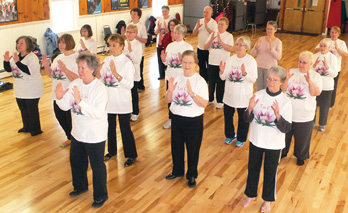 Photo shows a group of seniors standing in a room practicing Tai Chi.