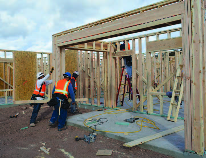 Photo shows construction workers framing a building.