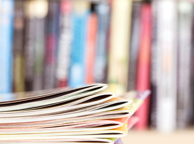 Closeup of a stack of colorful magazines with a bookshelf in the background.