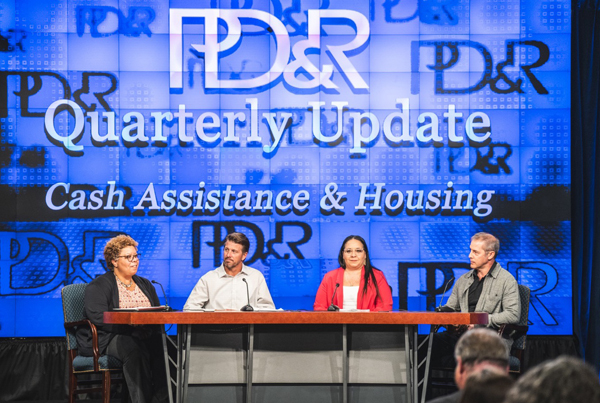Panelists sit at a table in discussion during the Quarterly Update Cash Assistance & Housing event.