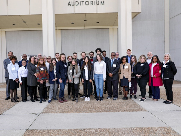 Photo of students, guest speakers, and HUD staff gathered in the plaza in front of an auditorium.