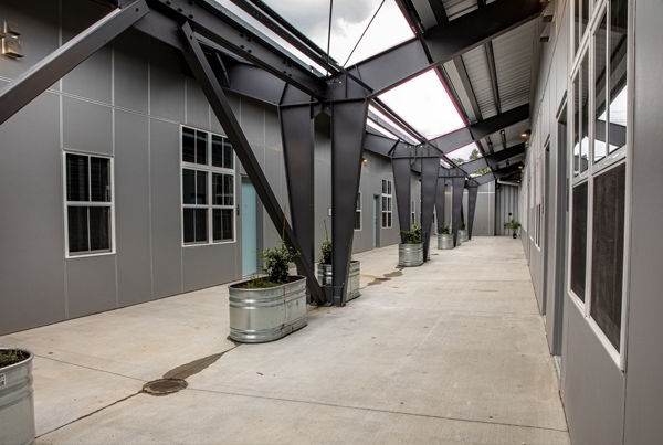 Image of a long, narrow courtyard formed by two one-story warehouse-style buildings.