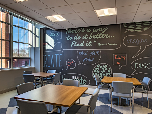 Photograph of a series of tables situated in front of a chalkboard wall with phrases and drawings.