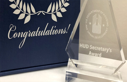 Photo of a blue box with the word “Congratulations!” and a plaque saying “U.S. Department of Housing and Urban Development” and “HUD Secretary’s Award”.
