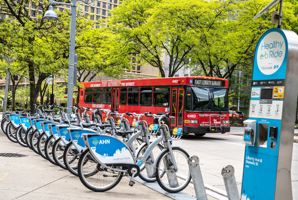 A bike share station with a row of bikes and a public bus in the background.