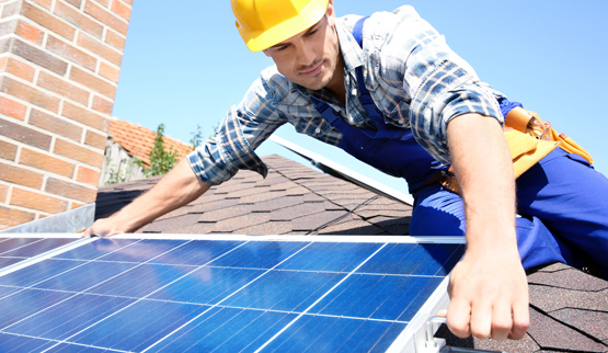 Photograph of a man installing a solar panel on a shingled roof.