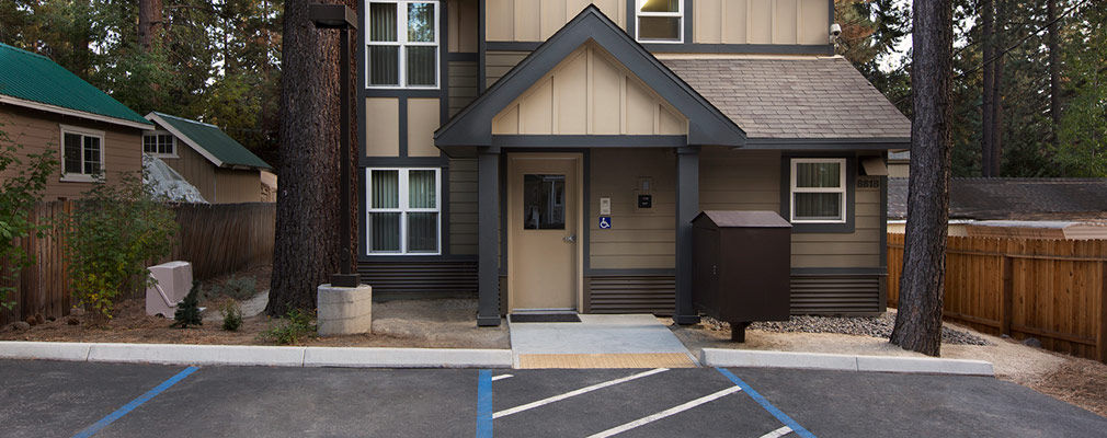 Photograph of the front façade of a two-story, front-gabled building with wood siding. The front door is accessible from the parking area in front of the house.