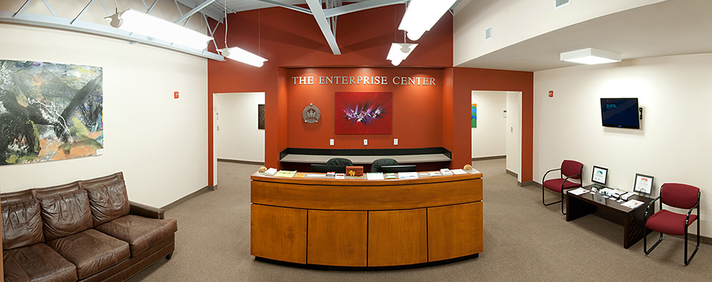 Photograph of the lobby of the Enterprise Center, furnished with a wood-paneled reception desk, a leather sofa, chairs, and a side table with reading material. 