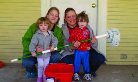A mother and three girls sitting on their front stoop with a mop and cleaning materials.