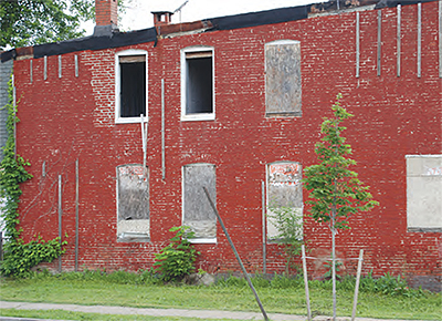A brick building in deteriorating condition with boarded up and broken windows. 