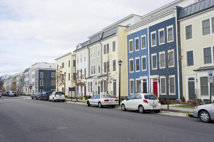 A row of townhomes with cars parked on the street. Image