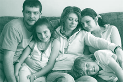 A picture of a family of five sitting close together on a sofa.