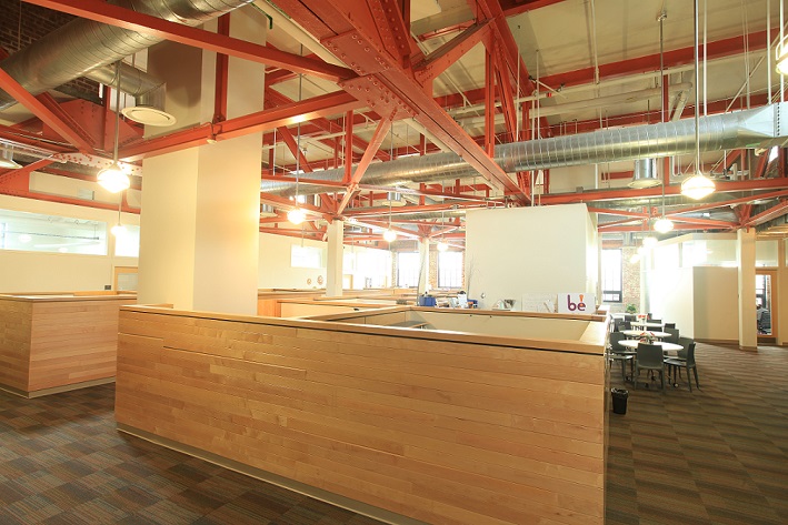 Photograph of the inside of the Business Development Incubator at New Jersey City University showing an open floor plan with cubicle partitions. Exposed rafters and mechanical systems create an open and airy space.