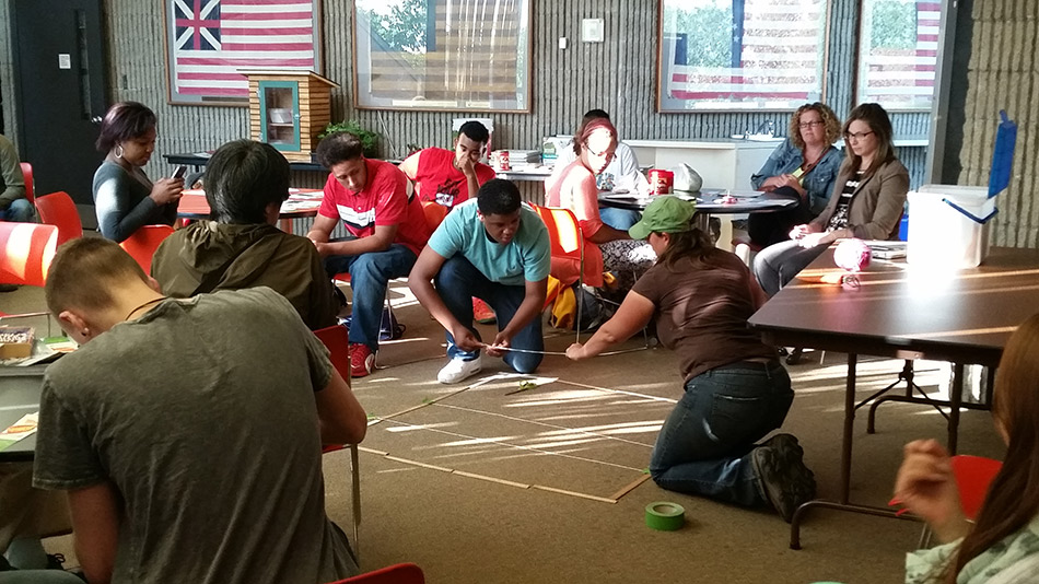 Photograph of a dozen young adults at tables in a large room designing gardening containers.