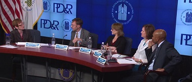Photograph of Assistant Secretary for Policy Development and Research Katherine O'Regan and four panelists at a table on stage in front of banners displaying the HUD and PD&R logos.