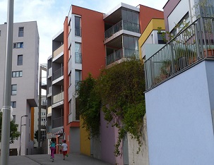 Photograph of one of the walkways of the Kabelwerk housing community. Children are playing outside, and bushes and brightly colored building walls line the walkway.