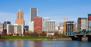 Photograph of the Portland, Oregon skyline during the day including several multi-story buildings, the Willamette River, and the Hawthorne Bridge.