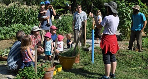  Image of Justina Gonzalez, co-founder of a children’s themed Common Ground garden, speaking to a group of parents and children about the vegetables in the garden before embarking on “The Great Veggie Hunt.” 