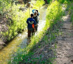 Three students walking along an acequia.