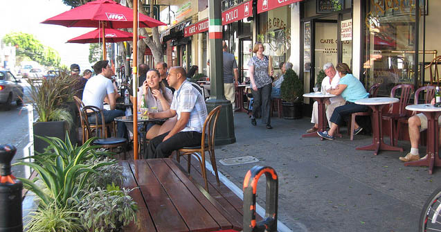Café sidewalk scene with people, tables, and umbrellas