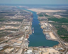 A low-altitude aerial photograph looking east at the Port of Brownsville in the foreground and the canal leading to the Gulf of Mexico in the distance.