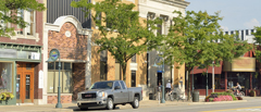 Photograph of contiguous buildings along a street. The building facades feature different materials and colors, and the street is lined by sidewalks and trees.