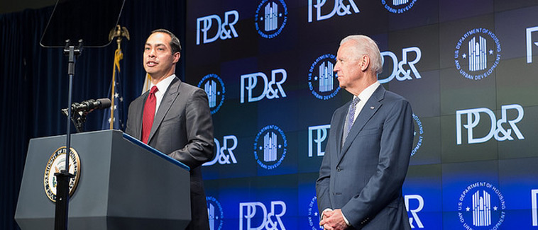 Photograph of HUD Secretary Julián Castro speaking at a podium onstage, with Vice President Joe Biden standing to his left, in front of a backdrop with the HUD and PD&R logos.