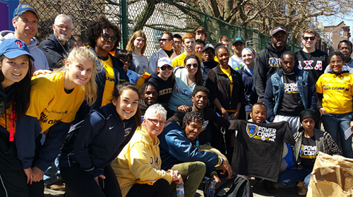 Photograph of more than 30 individuals, some displaying shirts with the logo, 'Power Corps,' gathered outside.