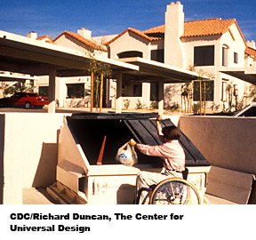 A woman in a wheel chair is utilizing an accessible trash dumpster.