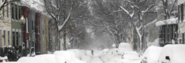 Snow covered residential block with cars lining each side of the street.