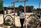 Native American woman standing at gate in front of home.