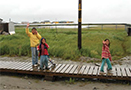 Three children walking across wooden path.