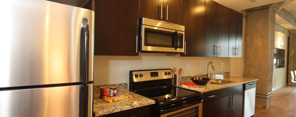 Photograph of the interior of an apartment showing the kitchen, which features stainless steal appliances and granite countertops.