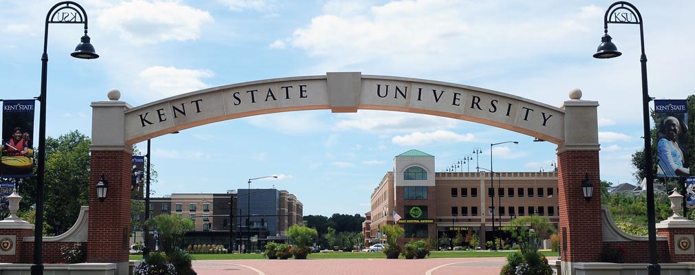 Photograph of an archway with the words “Kent State University,” with new multistory buildings in the background.