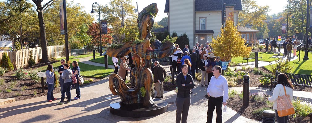 Photograph of groups of people talking near a sculpture behind a three-story residential building.