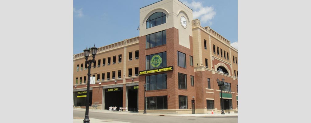 Photograph of the front and side façades of a three-story masonry building, with commercial space on the ground floor of the front façade and wide bays on the side façade to structured parking for buses and automobiles.