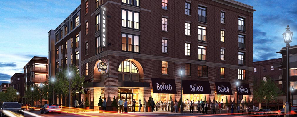 Photograph taken at dusk of the two street façades of a corner, four-story masonry building, with commercial uses on the ground floor and residential units in the upper stories.