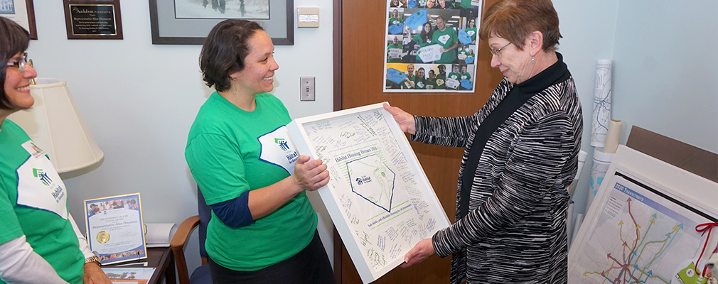 Two women hold a framed poster with signatures while a third women looks on.