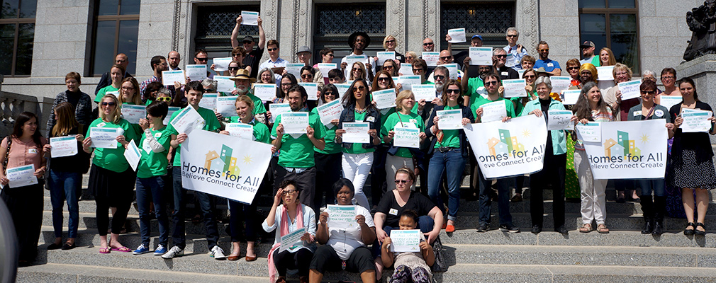 A group of people holding banners and certificates stand on steps in front of a building.