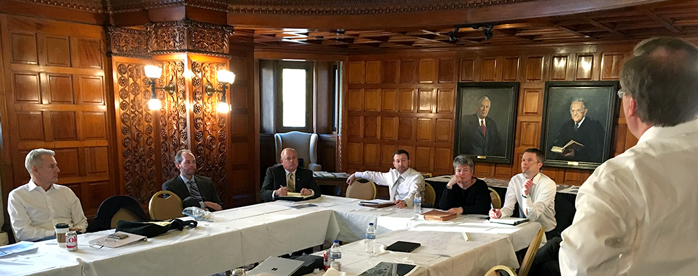 Five men and one woman seated at tables participate in a discussion.