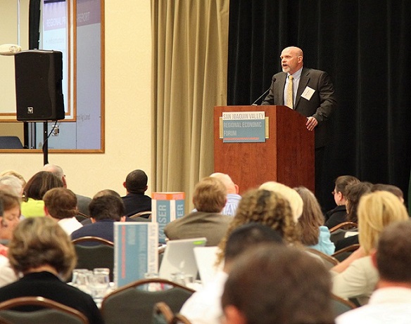 Photograph of Mike Dozier, executive director of OCED, speaking into a microphone in front of a group of seated individuals at the San Joaquin Valley Regional Economic Forum.