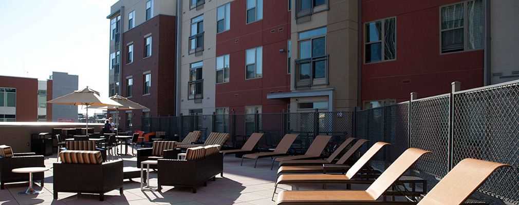 Photograph of a terrace behind one of the U Square @ the Loop buildings furnished with reclining pool chairs and arm chairs arranged around tables.