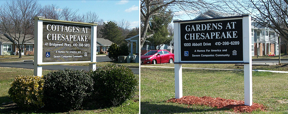 Two photographs taken at ground level of the freestanding signs for the Cottages at Chesapeake and the Gardens at Chesapeake located in a lawn area at the entrances to the respective developments. Each sign is about three feet high by five feet wide elevated above the ground about four feet on two posts. Buildings in the developments are in the background.