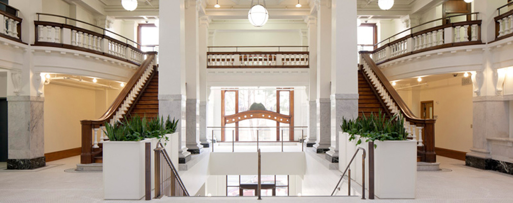Photograph taken within the lobby across the top of the grand staircase toward large windows in the background.