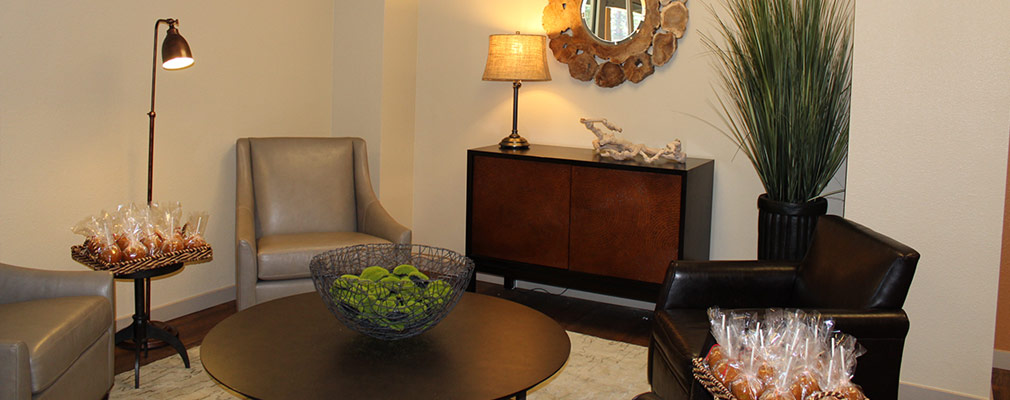 Photograph of a corner of a community room with upholstered chairs arranged around a circular coffee table.