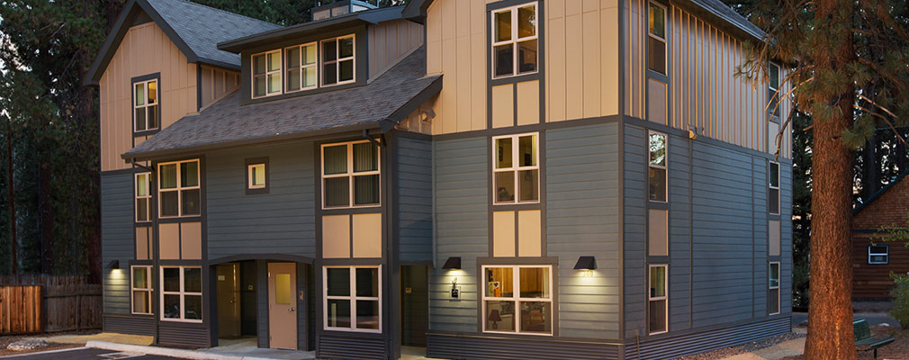 Photograph of the front façade of a three-story building with wood siding. The central portion of the façade extending in front of the rest of the façade is capped with a roof pitched toward the front; a dormer with three windows has a similarly pitched roof. Gables mark the two corner sections of the façade.