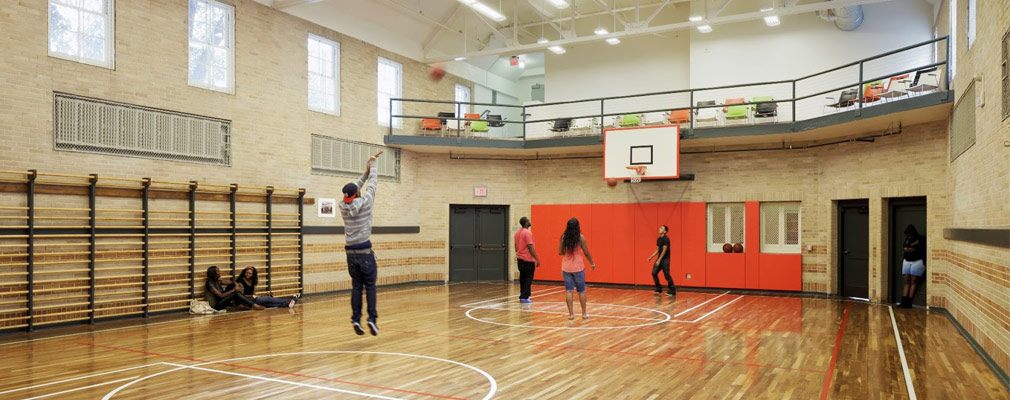 Photgraph showing young adults and children playing on an indoor basketball court.