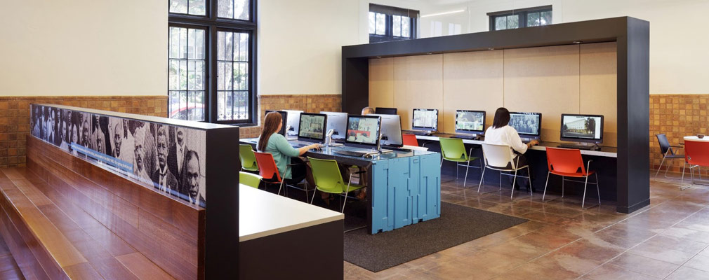 Photograph of the three people sitting at computers in a room of eleven computers. The mural bench forms a partial wall for the computer area.