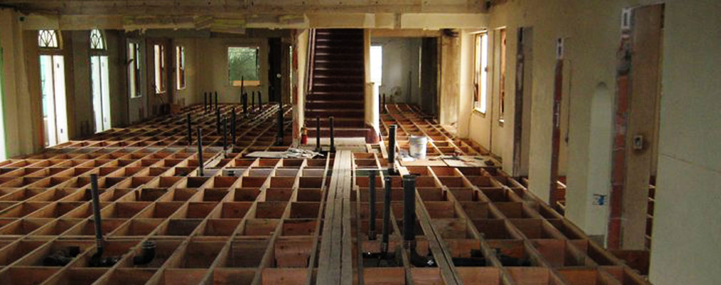 Photograph of a room with exposed floor joists and pipes.