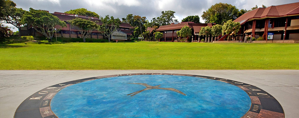 Photograph of a large compass installed in a lawn ringed by university buildings.